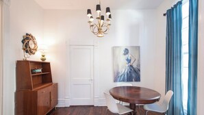 A dining area with a round table, white chairs, a wooden cabinet, a chandelier, and a painting on the wall. - Relaxing Apt near Cherokee Park and Frankfort Ave! (Louisville)