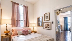 A bedroom with a bed, bedside lamps, a window with curtains, and framed pictures on the wall. - Relaxing Apt near Cherokee Park and Frankfort Ave! (Louisville)