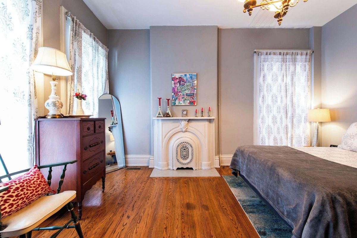 Un dormitorio con cama, cómoda, chimenea y ventana con cortinas.
