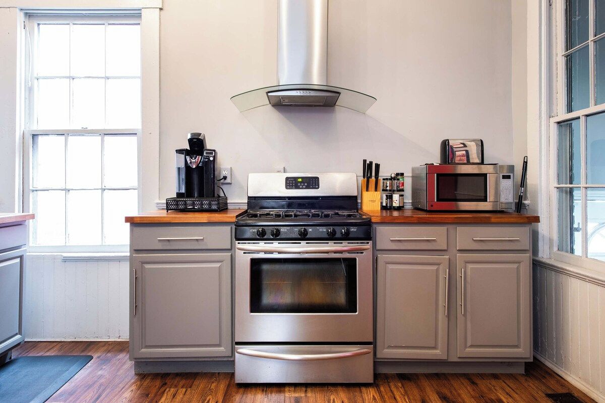 Una cocina con estufa de acero inoxidable, un microondas y una cafetera sobre la encimera.