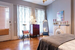 A bedroom with a bed, a dresser, a chair, a mirror, a fireplace, and curtains.
