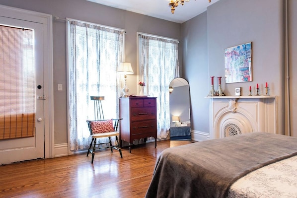 A bedroom with a bed, a dresser, a chair, a mirror, a fireplace, and curtains.