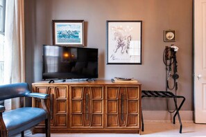 A living room with a TV on a wooden cabinet, a blue chair, and two framed pictures on the wall.