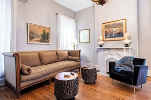 A living room with a sofa, a chair, two round wooden side tables, and a fireplace with a mantle.