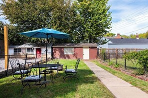 A backyard with a table and chairs, a blue umbrella, and a house in the background.