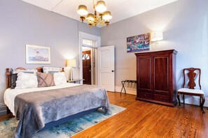 Quarto com cama, mesa de cabeceira, cômoda, cadeira e porta que dá para outro ambiente.