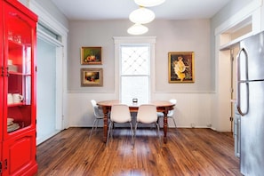 Uma sala de jantar com uma mesa e cadeiras de madeira, um armário vermelho e duas obras de arte emolduradas na parede.