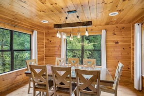 L’intérieur d’un chalet en bois, avec une table et des chaises, de grandes fenêtres et un luminaire au plafond.