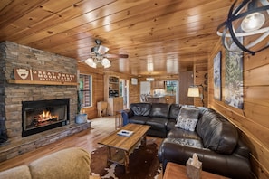 Un intérieur de chalet chaleureux avec une cheminée en pierre, un canapé en cuir, un plancher en bois et un coin repas.