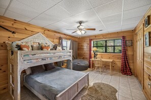 Ein blockhaushaftes Zimmer mit Etagenbett, Schreibtisch, Stuhl, Deckenventilator und einem fenster mit Vorhängen.