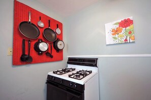 Uma cozinha com fogão a gás, um painel perfurado vermelho com utensílios de cozinha e um quadro com flores na parede.