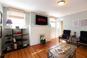 A living room with a fireplace, a flat-screen TV mounted above it, a coffee table with books, and two armchairs. - Vibrant Crescent Hill Apt close to Cherokee Park! (Louisville)