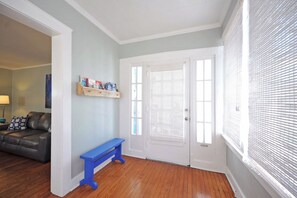 Une pièce avec un plancher en bois, un banc bleu, une porte blanche avec des stores et une bibliothèque adossée au mur.