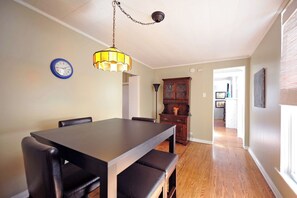 Uma sala de jantar com uma mesa e cadeiras de madeira, um lustre, um relógio e um armário.