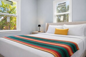 Ein Schlafzimmer mit einem Bett, einem Nachttisch, einer Lampe und einem Fenster mit Jalousien.
