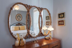 A bedroom with a large ornate mirror, a bed with white linens, and a dresser with decorative items. - Spacious 3BR Crescent Hill Apt | Yard & Parking (Louisville)