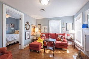 A cozy living room with a red sofa, a wooden coffee table, and a bed in the adjacent room. - Spacious 3BR Crescent Hill Apt | Yard & Parking (Louisville)