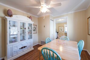 Un coin repas avec une table en bois et des chaises turquoise, un buffet blanc aux portes vitrées et un ventilateur de plafond.