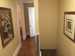 A hallway with wooden flooring, a white door at the end, and framed artwork on the walls. - Spacious 3BR Crescent Hill Apt | Yard & Parking (Louisville)