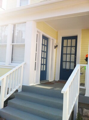 A residential building with a front porch, a set of stairs leading to the entrance, and a blue door. - Spacious 3BR Crescent Hill Apt | Yard & Parking (Louisville)