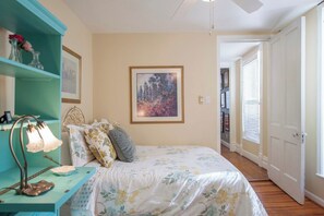 A bedroom with a bed, a nightstand, a wall-mounted lamp, a framed picture, and a door leading to another room. - Spacious 3BR Crescent Hill Apt | Yard & Parking (Louisville)