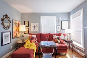 Un salon avec un canapé rouge, une table basse en verre et un plaid jaune.