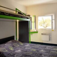 Una habitación con literas, un ventanal con vistas a árboles y un radiador.