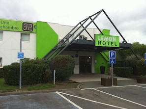 A hotel entrance with a green and white facade, a ramp for accessibility, and a parking sign indicating disabled parking. - Lemon Hotel - Tourcoing (Tourcoing)