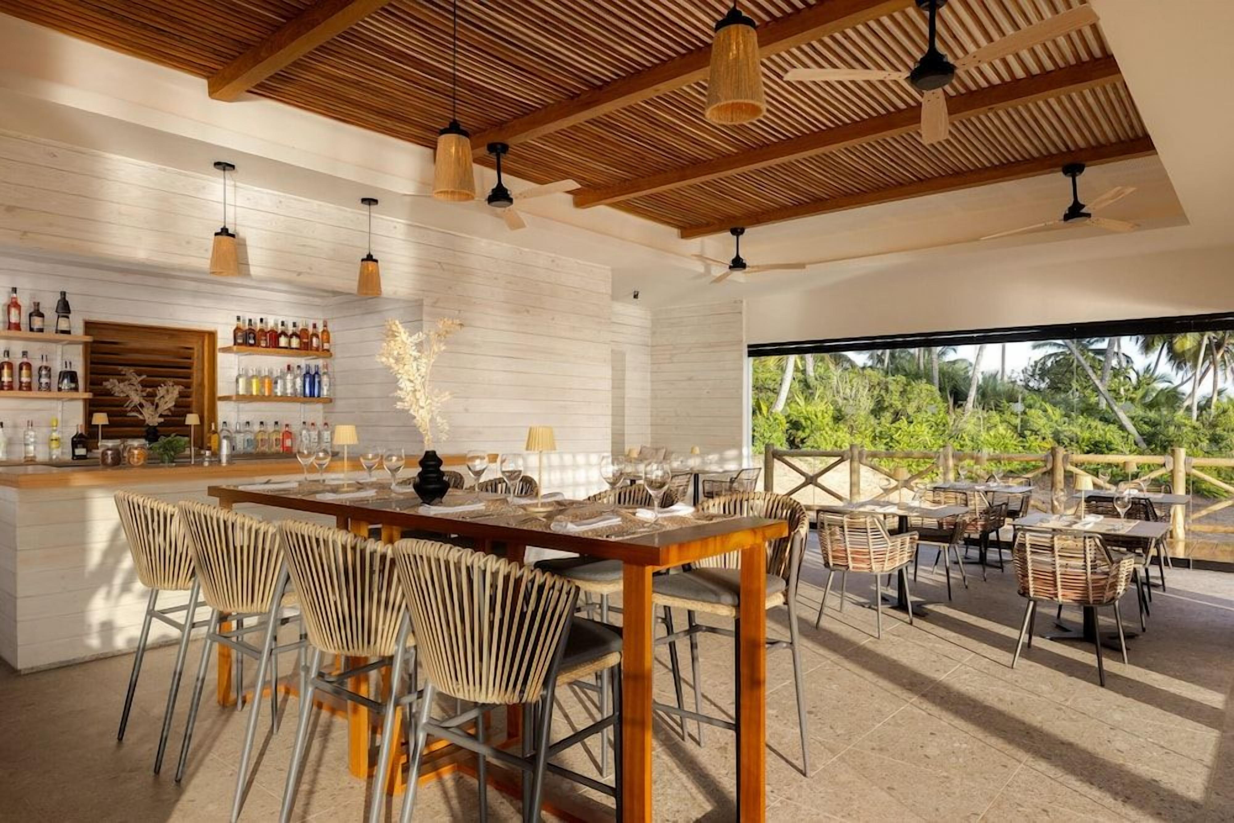 A modern bar area with a wooden ceiling, bar stools, and a variety of bottles.