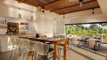 A modern bar area with a wooden ceiling, bar stools, and a variety of bottles.