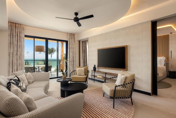 A modern hotel room with a large flat-screen TV, a ceiling fan, and a view of the ocean.