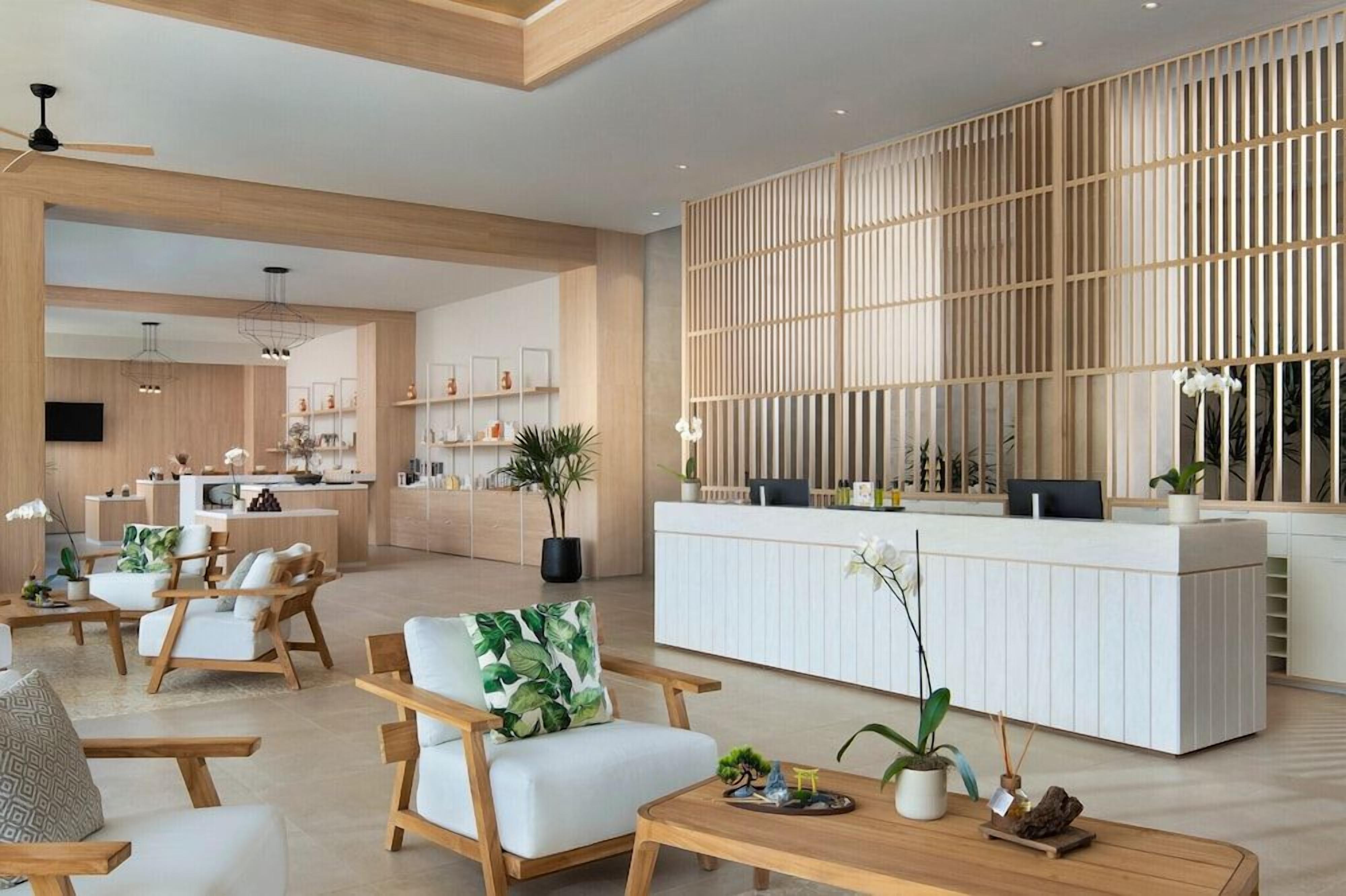 A modern hotel lobby with a reception desk, seating area, and a kitchen in the background.