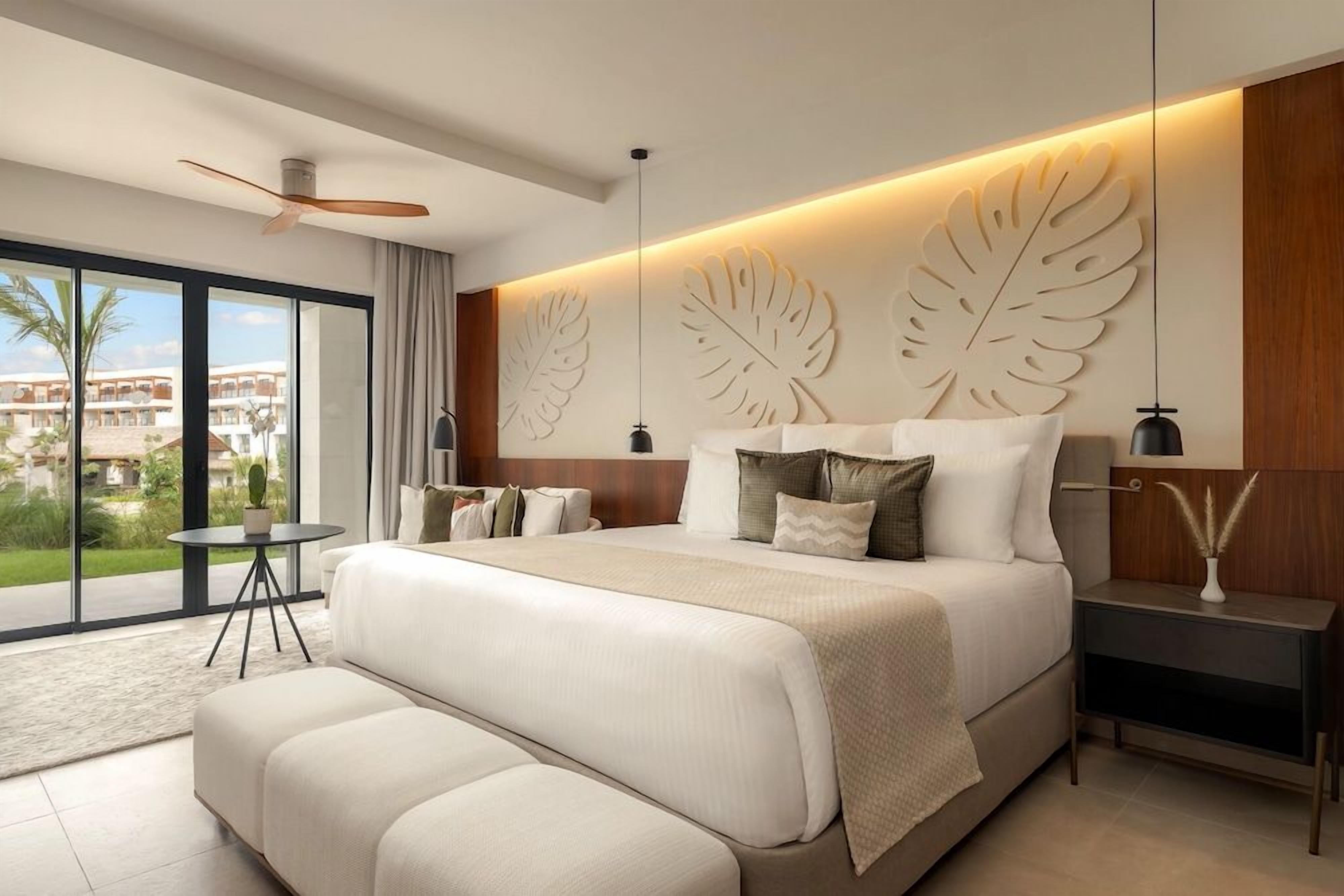 Une chambre à coucher moderne avec un grand lit, une table de chevet, une commode et une vue sur l’extérieur.