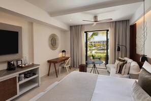 A hotel room with a bed, a desk, a TV, a chair, a small table, and a view of a pool and buildings.