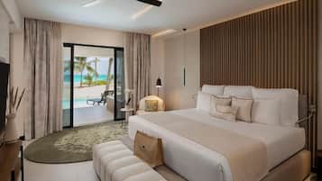 A hotel room with a large bed, a ceiling fan, a view of the beach, and a small table with a lamp.
