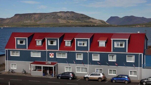 A multi-story hotel with a red roof, a visible entrance, and a parking area with cars. - Framnes (Grundarfjörður)