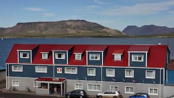 A multi-story hotel with a red roof, a visible entrance, and a parking area with cars.