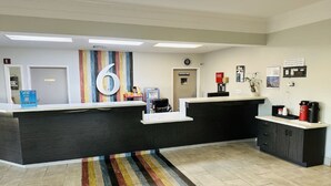 A reception area with a large number '6' on the wall, a counter, a coffee machine, and a small plant. - Motel6 Mobile, AL Airport Blvd (Mobile)