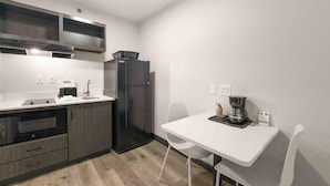 A compact kitchen with a microwave, oven, refrigerator, and a small dining table with chairs. - Motel6 Mobile, AL Airport Blvd (Mobile)