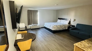 A hotel room with a bed, a sofa, a desk with a chair, a television, and a window with curtains. - Motel6 Mobile, AL Airport Blvd (Mobile)