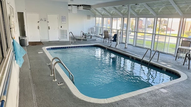An indoor swimming pool with clear water, surrounded by a covered area with chairs and a view of the outdoors. - Motel6 Mobile, AL Airport Blvd (Mobile)