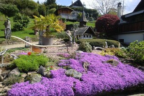 A garden with purple flowers, a palm tree, and a small house with a balcony. - Holiday apartment with 2 bedrooms (Sasbachwalden)