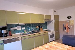 A compact kitchen with green cabinets, a sink, a stove, and a coffee maker. - Holiday apartment with 2 bedrooms (Sasbachwalden)