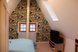 A bedroom with a sloped ceiling, a bed, a TV on a wooden stand, and a window with a lattice screen. - Holiday home with 4 bedrooms (Hundsdorf)