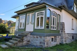 Een huis met een stenen fundering, een geel-wit gevel en een trap die naar de ingang leidt.