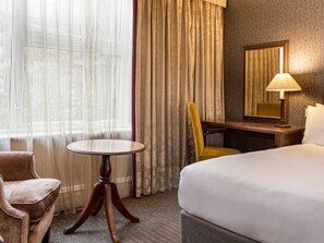 Habitación de hotel con cama, una mesa redonda, una silla, un escritorio, una lámpara y un espejo.