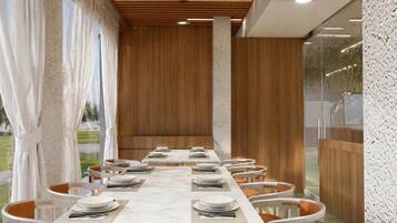 Un comedor moderno con una mesa larga dispuesta para varios comensales, paneles de madera en las paredes y vistas al exterior.