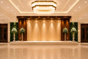 A spacious lobby with a stage, a large chandelier, and decorative floral arrangements. - The Laali Imperial (Amravati)
