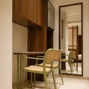 A room with a wooden cabinet, a television mounted on the wall, and a mirror reflecting a bed and a chair. - The Laali Imperial (Amravati)