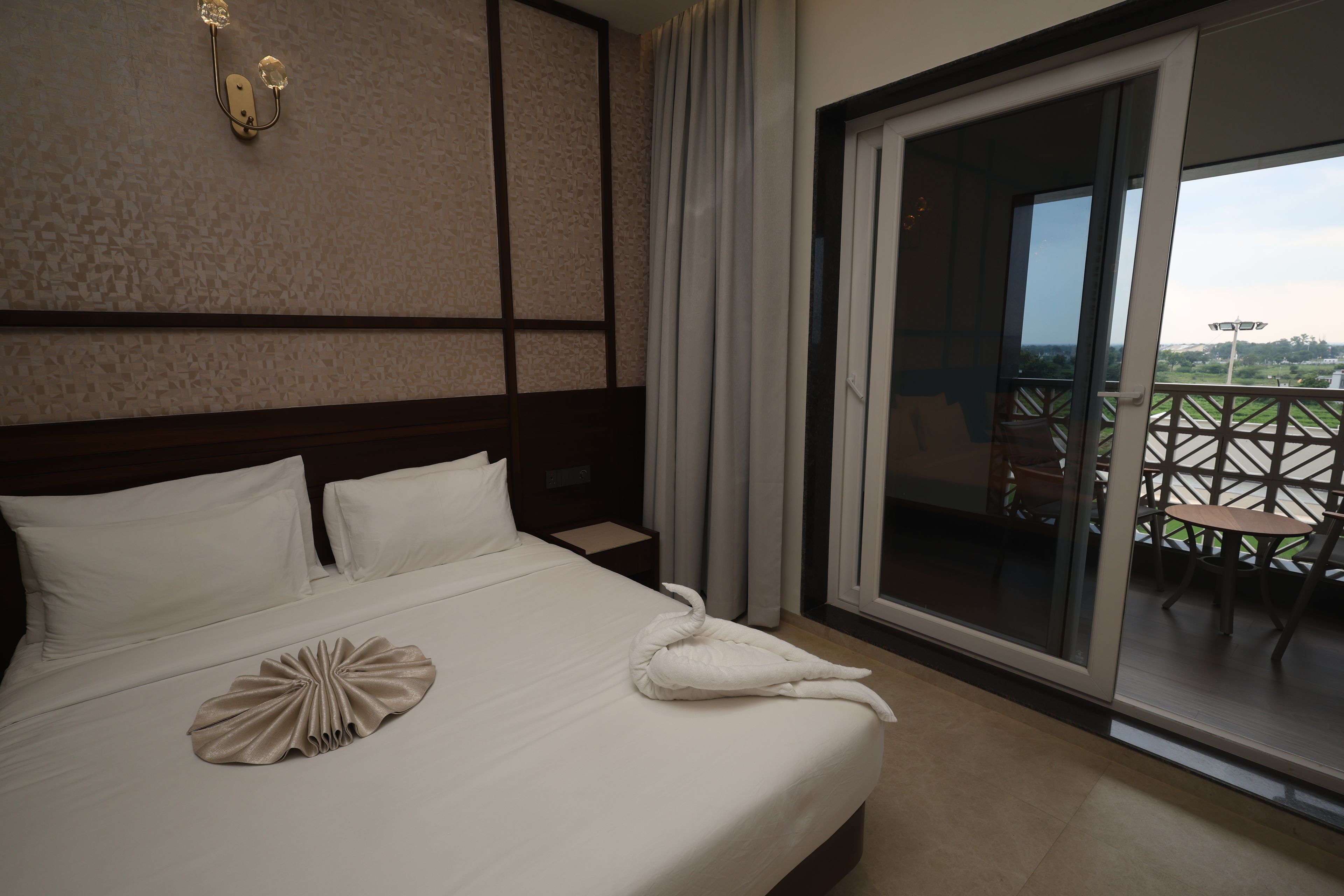 Habitación de hotel con una cama grande, vistas al exterior y un balcón con mobiliario.